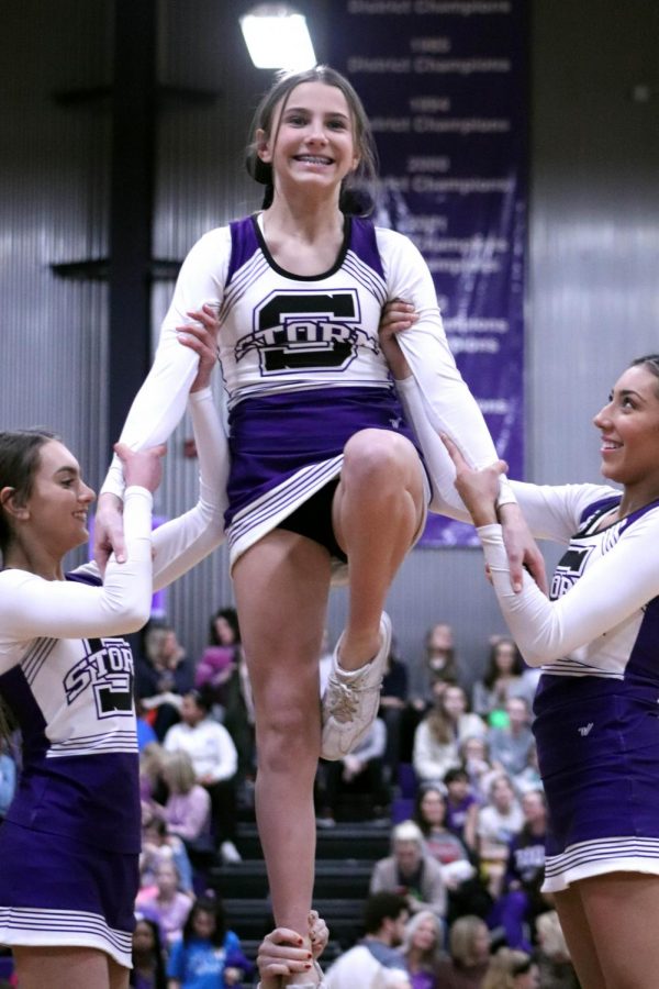 Senior Meg Wilkerson and junior Bella Aquino hold freshman Emily Dierks as she nods at the crowd during cheers halftime performance Feb. 27.