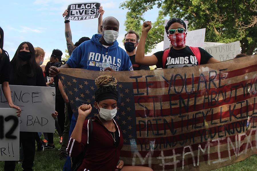 Three protesters hold an American flag being used as a protest sign and raise fists during the Black Lives Matter demonstration at the J.C. Nichols Memorial Fountain on May 30. A raised fist is a symbol commonly used to represent solidarity among oppressed peoples.