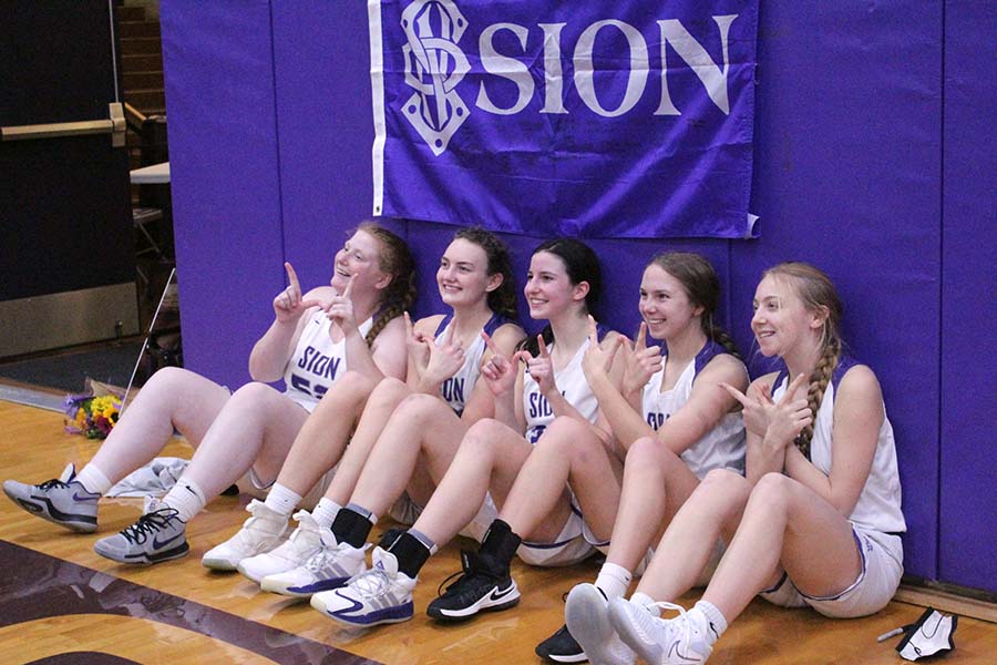 The five senior varsity players make the W with their hands under the Sion flag after winning their senior night game.