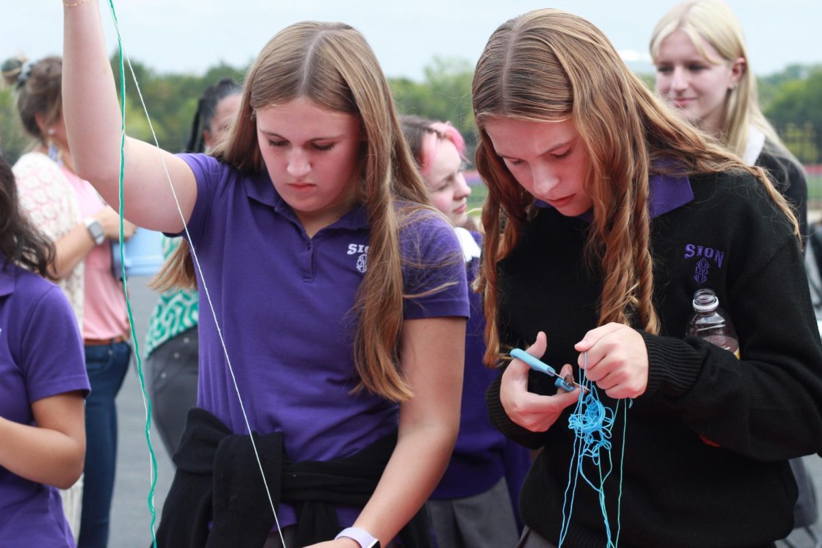 Freshmen Claire Weber and Nora Miller detangle thread to make each other bracelets. As freshmen, this was the first time they had attended an all-school celebration like this.