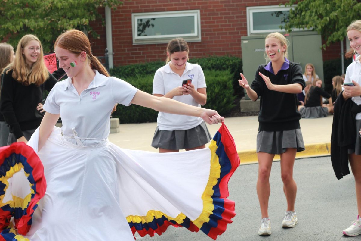 Senior Ava Townsend cheers on her friend senior Livvy Cavaliere as she dances in a circle skirt. Both seniors are members of the Sion dance team. 