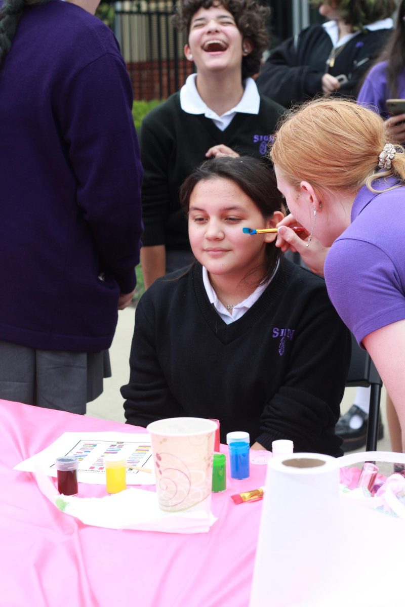 Spanish club member Ella Satterwhite paints a blue stripe on freshman Abigail Guerra’s cheek. Sion’s Spanish club ran a face paint table this year which was very popular. 