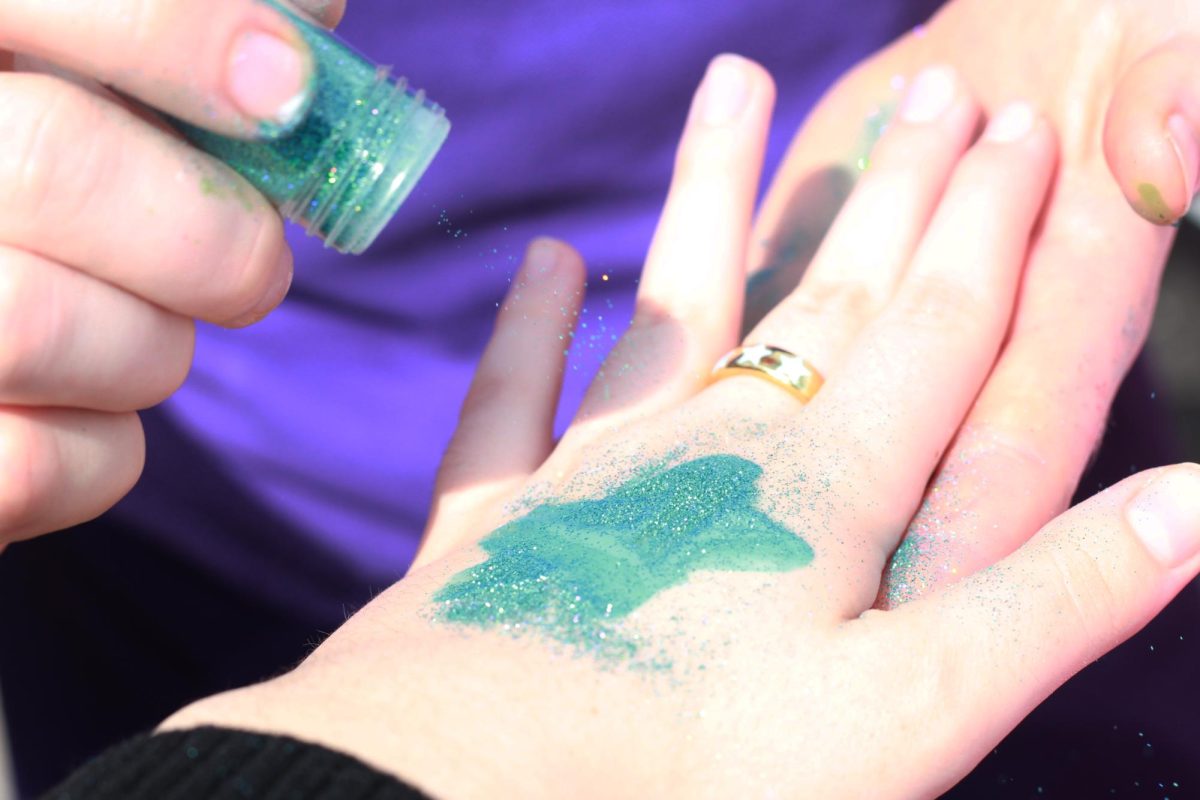 Junior Ella Satterwhite applies glitter to a blue star she painted on her friend’s hand. Satterwhite is a member of Sion’s Spanish club, which ran a face paint table at the event.