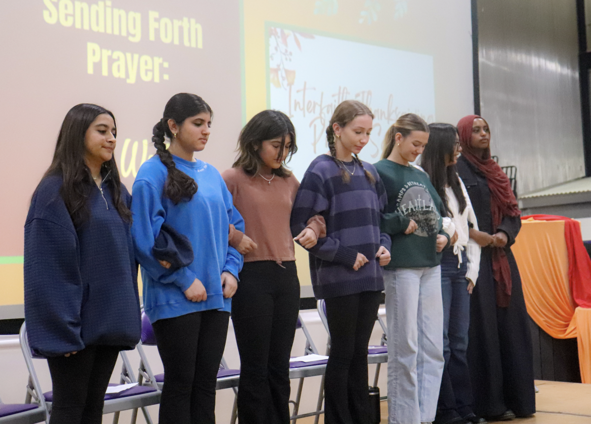 Bowing their heads, the Interfaith Prayer Service speakers link arms during the closing prayer November 16. Students from all thee abrahamic religions spoke to the school about their religion and experiences.