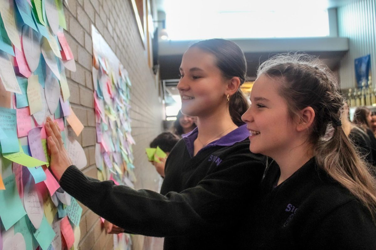 Posting their sticky notes, Freshmen Maggie Grilliot and Ella Gamper celebrate Founders Day Jan 18. Their notes reflect on a video they watched about the life of the school's founders. "I liked that we got to share our thoughts and opinions. It was a very community building activity," Grilliot said.